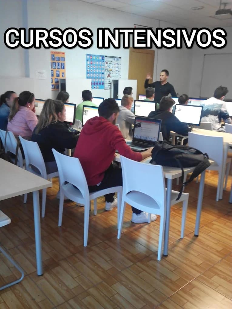 Estudiantes en aula de autoescuela con ordenadores y profesor bajo el título cursos intensivos.